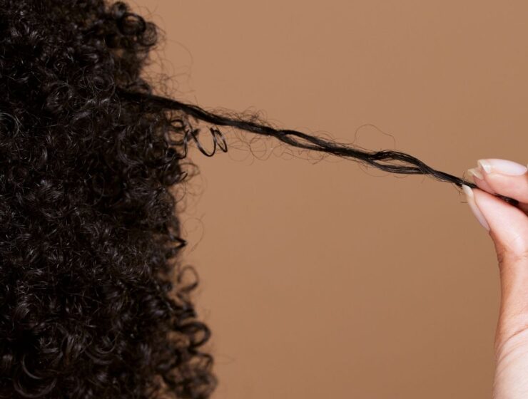 Hand gently stretching a single curl from dense curly hair.