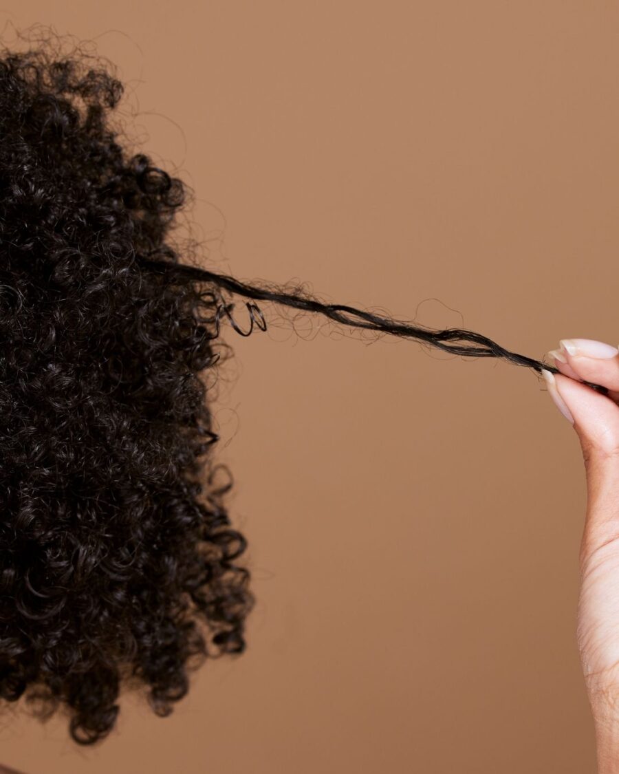Hand gently stretching a single curl from dense curly hair.