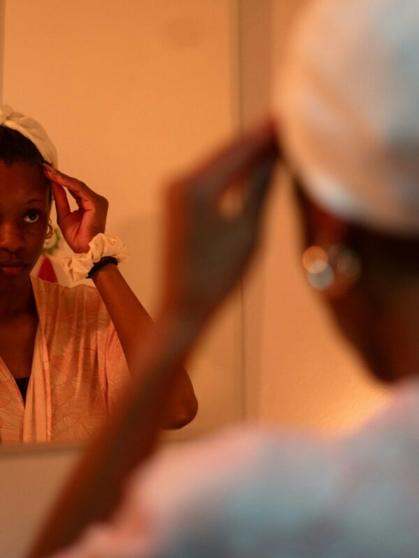 Woman looking in the mirror with a deep conditioner cap on her head.