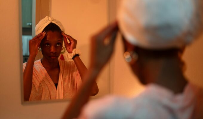 Woman looking in the mirror with a deep conditioner cap on her head.