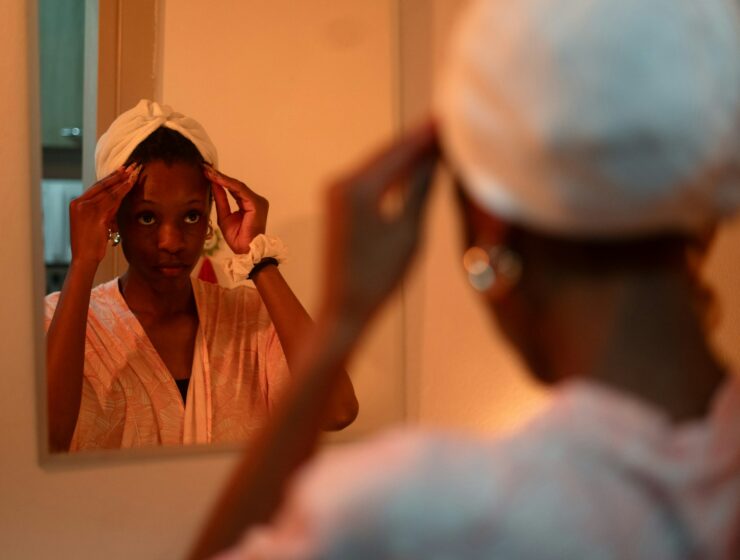 Woman looking in the mirror with a deep conditioner cap on her head.