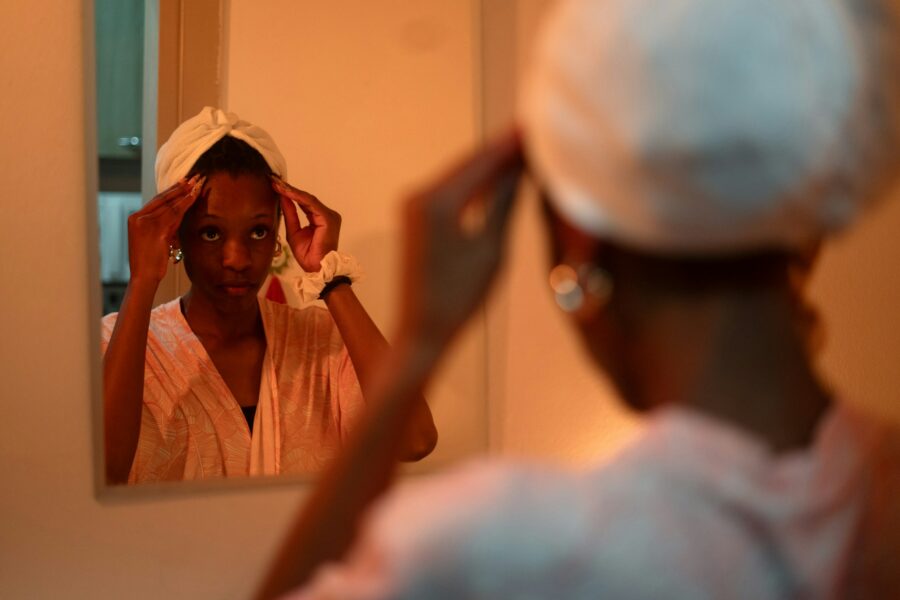 Woman looking in the mirror with a deep conditioner cap on her head.