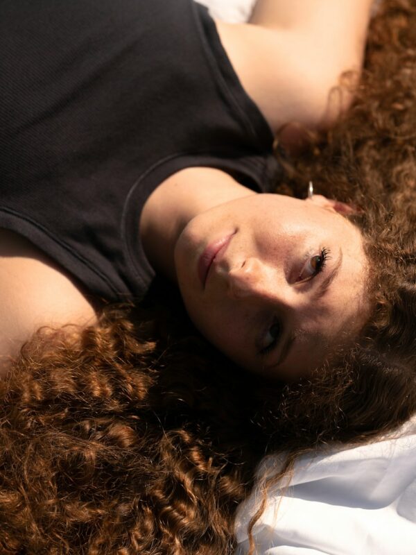 Woman with big curly hair laying on a bed.