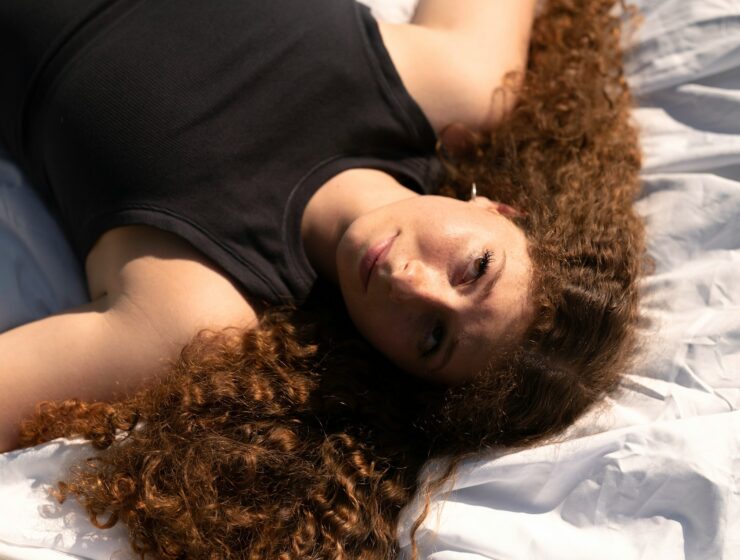 Woman with big curly hair laying on a bed.