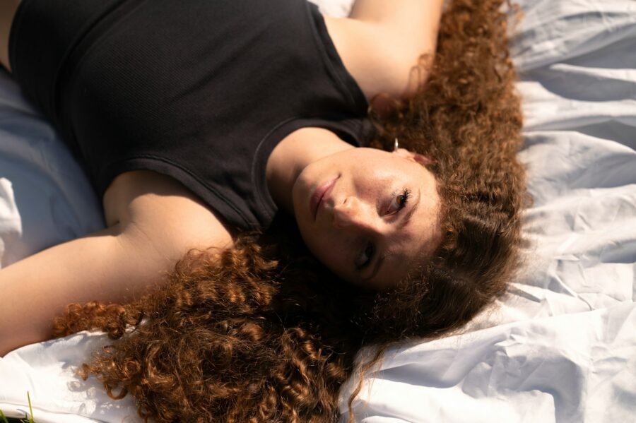 Woman with big curly hair laying on a bed.