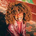 Woman with red curly hair, red glasses and a red jacket.