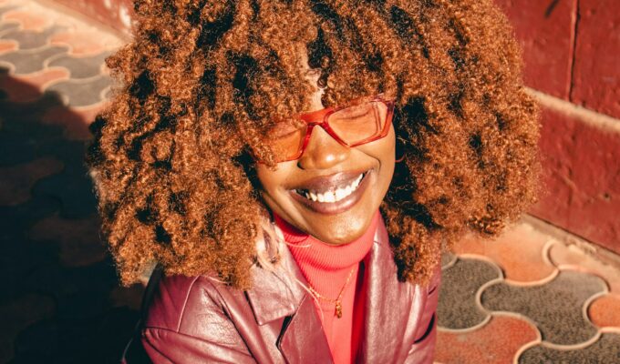 Woman with red curly hair, red glasses and a red jacket.