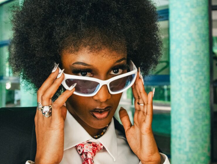 Woman with curly hair, wearing a suit and white sunglasses.