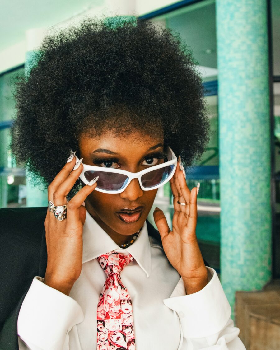 Woman with curly hair, wearing a suit and white sunglasses.