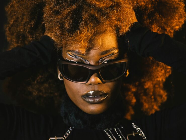 Woman posing with black sunglasses and a black outfit. Her hands are pushing the sides of her hair back.