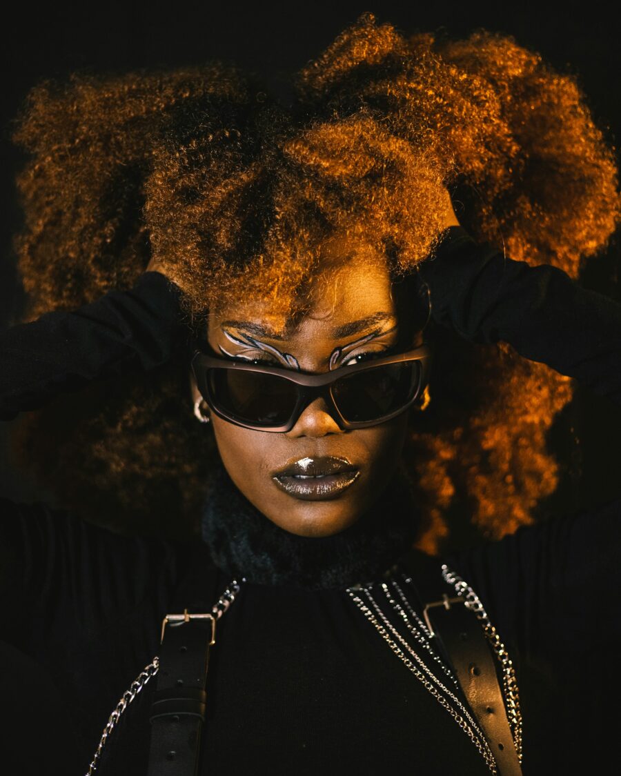 Woman posing with black sunglasses and a black outfit. Her hands are pushing the sides of her hair back.