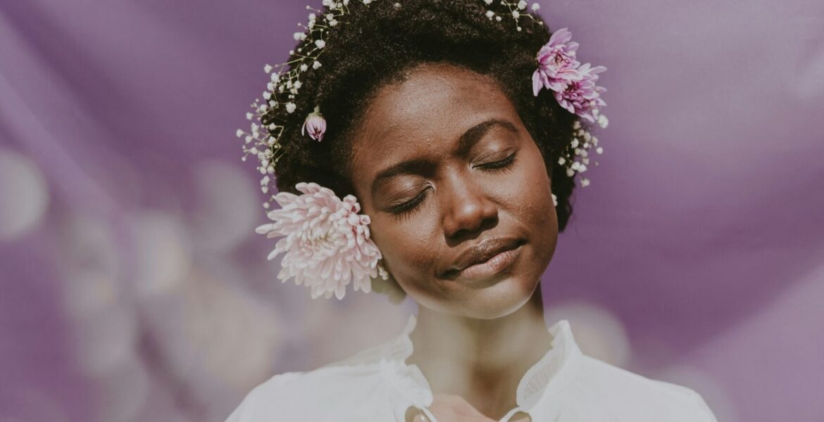 Woman posing with flowers in her curly, coily hair.