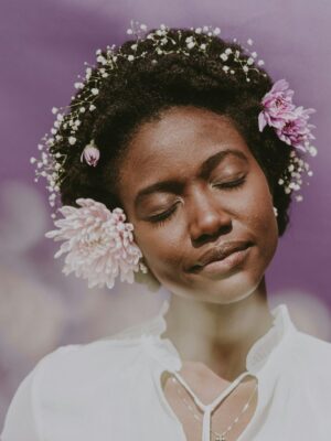 Woman posing with flowers in her curly, coily hair.