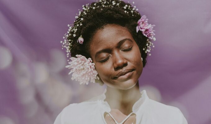 Woman posing with flowers in her curly, coily hair.