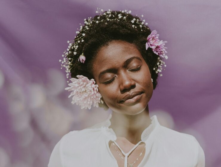 Woman posing with flowers in her curly, coily hair.
