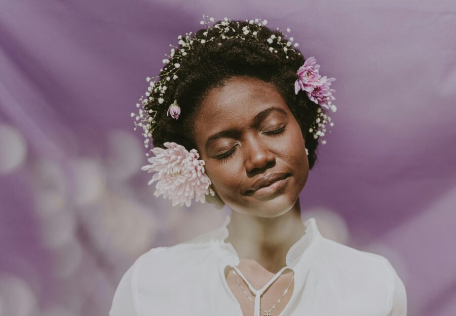 Woman posing with flowers in her curly, coily hair.