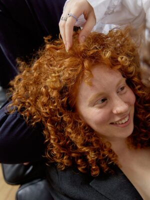 Woman with curly hair sitting on a chair.