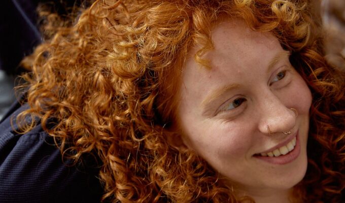 Woman with curly hair sitting on a chair.
