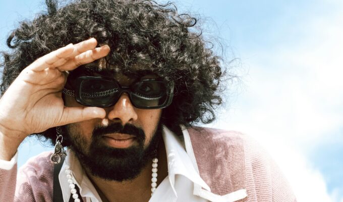 Man with big curly hair wearing sunglasses.