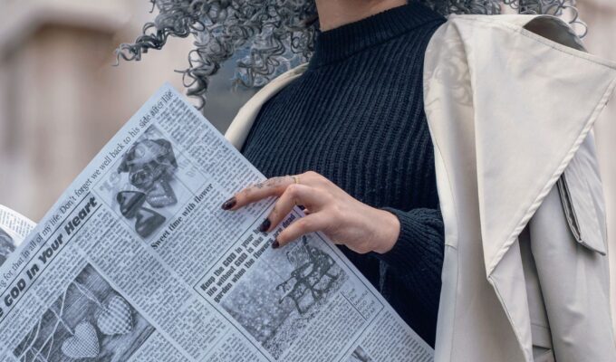 Woman with grey hair, holding a newspaper.