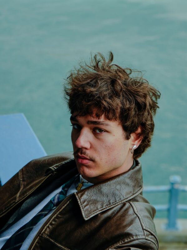 Man with curly hair wearing a leather brown jacket.