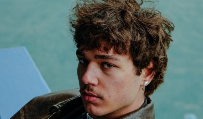 Man with curly hair wearing a leather brown jacket.