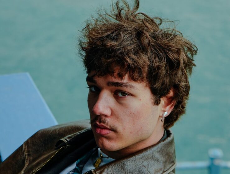 Man with curly hair wearing a leather brown jacket.