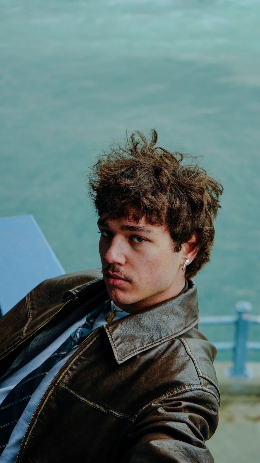 Man with curly hair wearing a leather brown jacket.