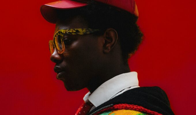 Side of a man's face, wearing a red hat, in front of a red background.