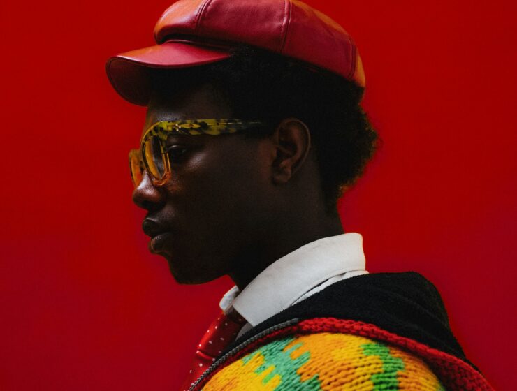Side of a man's face, wearing a red hat, in front of a red background.
