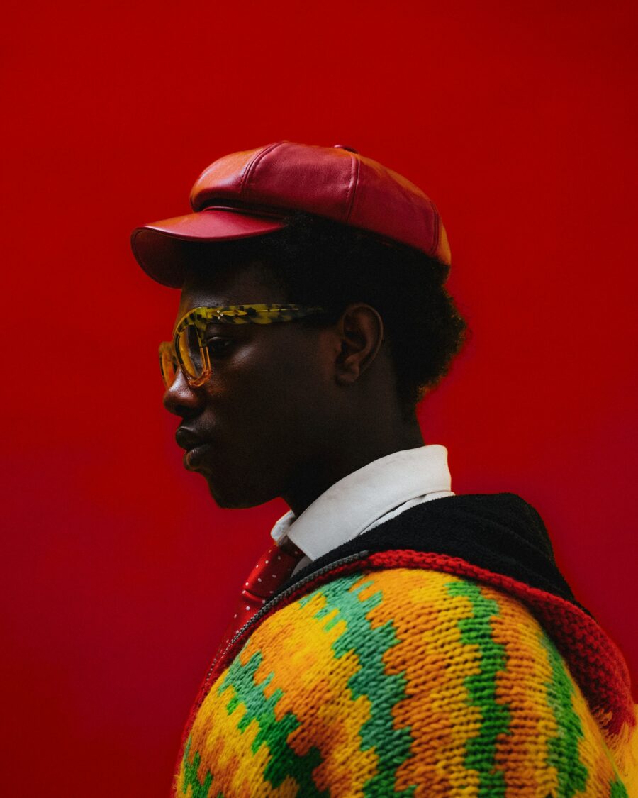 Side of a man's face, wearing a red hat, in front of a red background.
