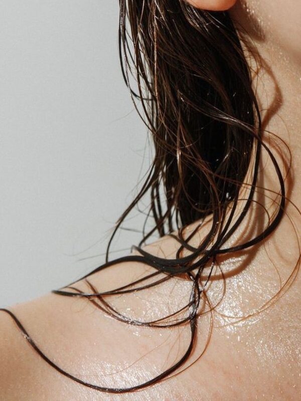 A close up of a woman's shoulder with wet curly hair.