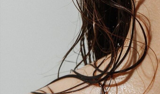 A close up of a woman's shoulder with wet curly hair.