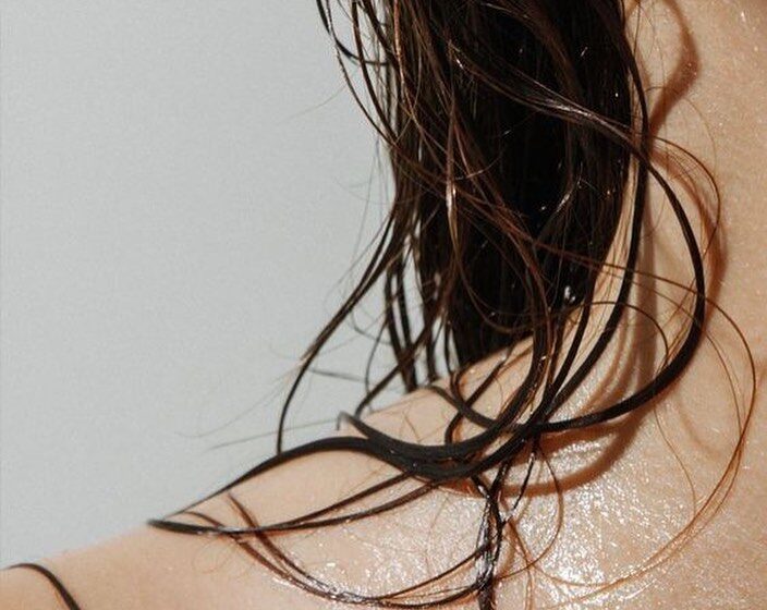 A close up of a woman's shoulder with wet curly hair.