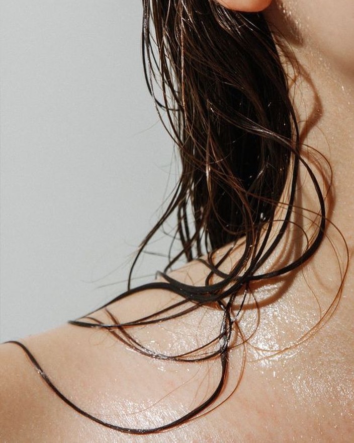 A close up of a woman's shoulder with wet curly hair.